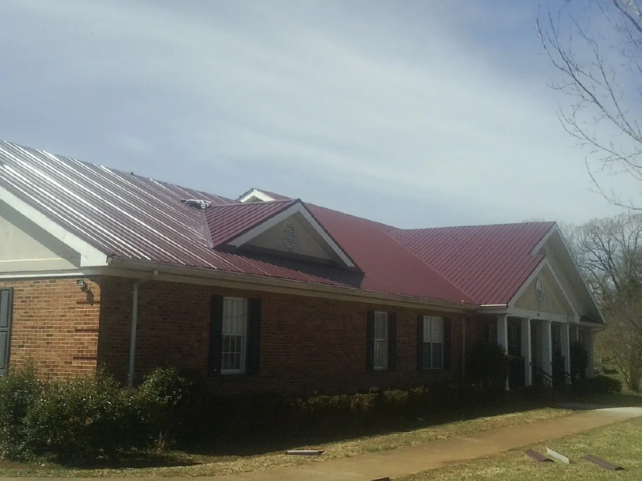 Red metal roof with gabled entries on a long brick building, from a Hail Damage Roof Repair job in Sanbornton