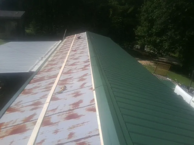 Old rusted panels beside newly installed green metal roofing — Wind Damage Roof Repair by Roofing Brothers in Sanbornton