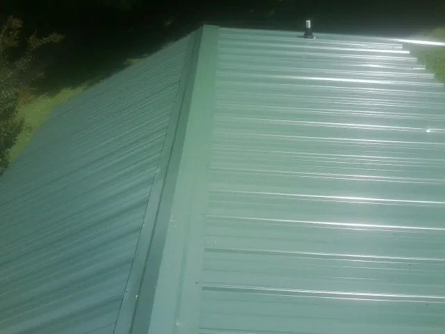 New green metal panels meeting at the ridge of a roof — Flat Roof Repair work by our crew in Sanbornton