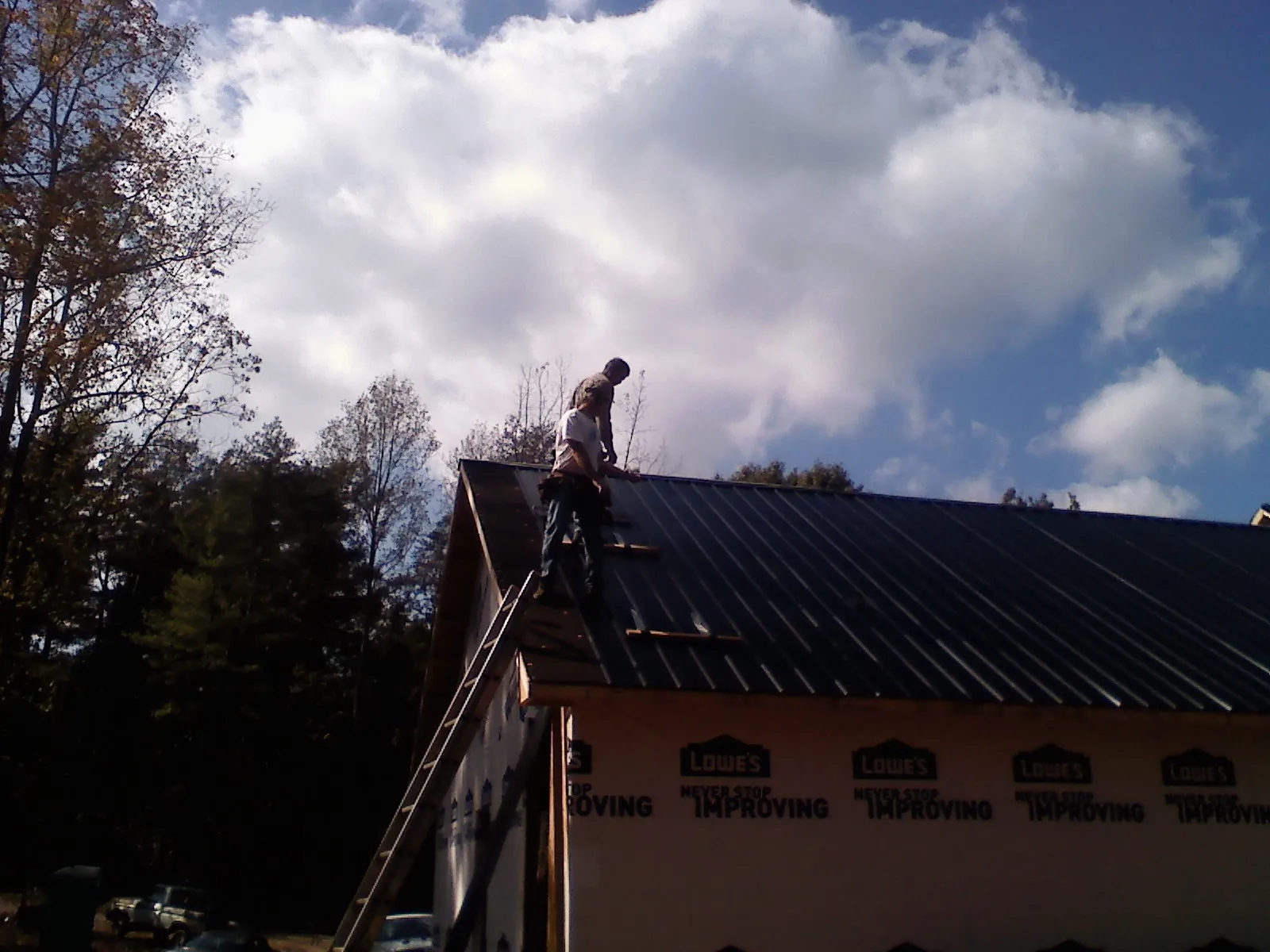 Roofer fastening dark metal panels high against a cloudy sky, from a Roof Inspection job in Sanbornton