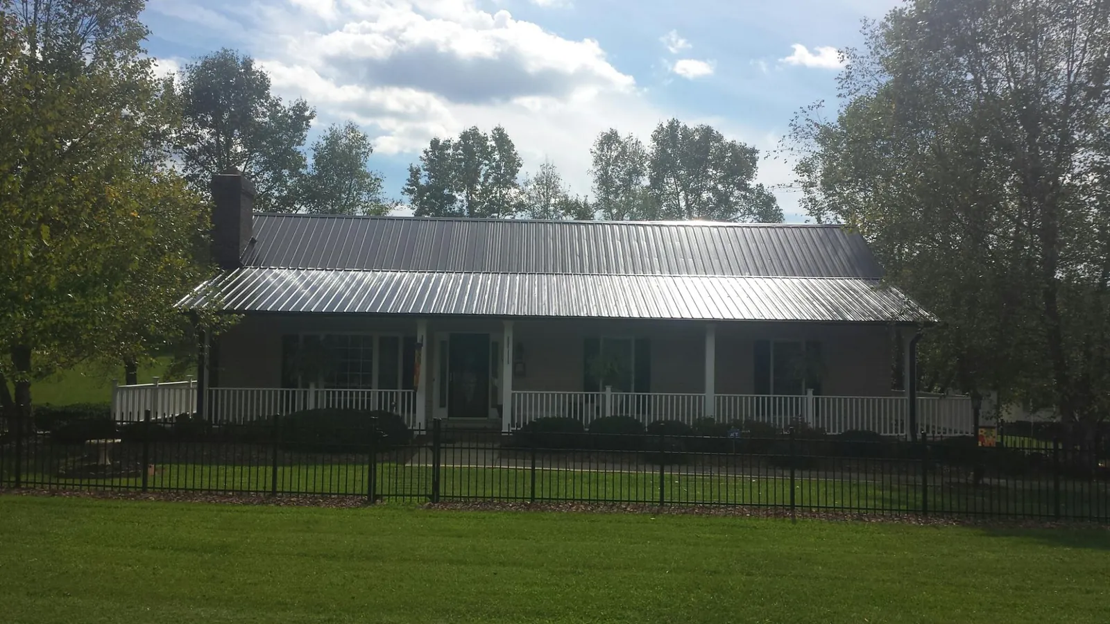 Gray metal roof on a brick ranch with a full width front porch — Gutter Guard Installation work by our crew in Sanbornton