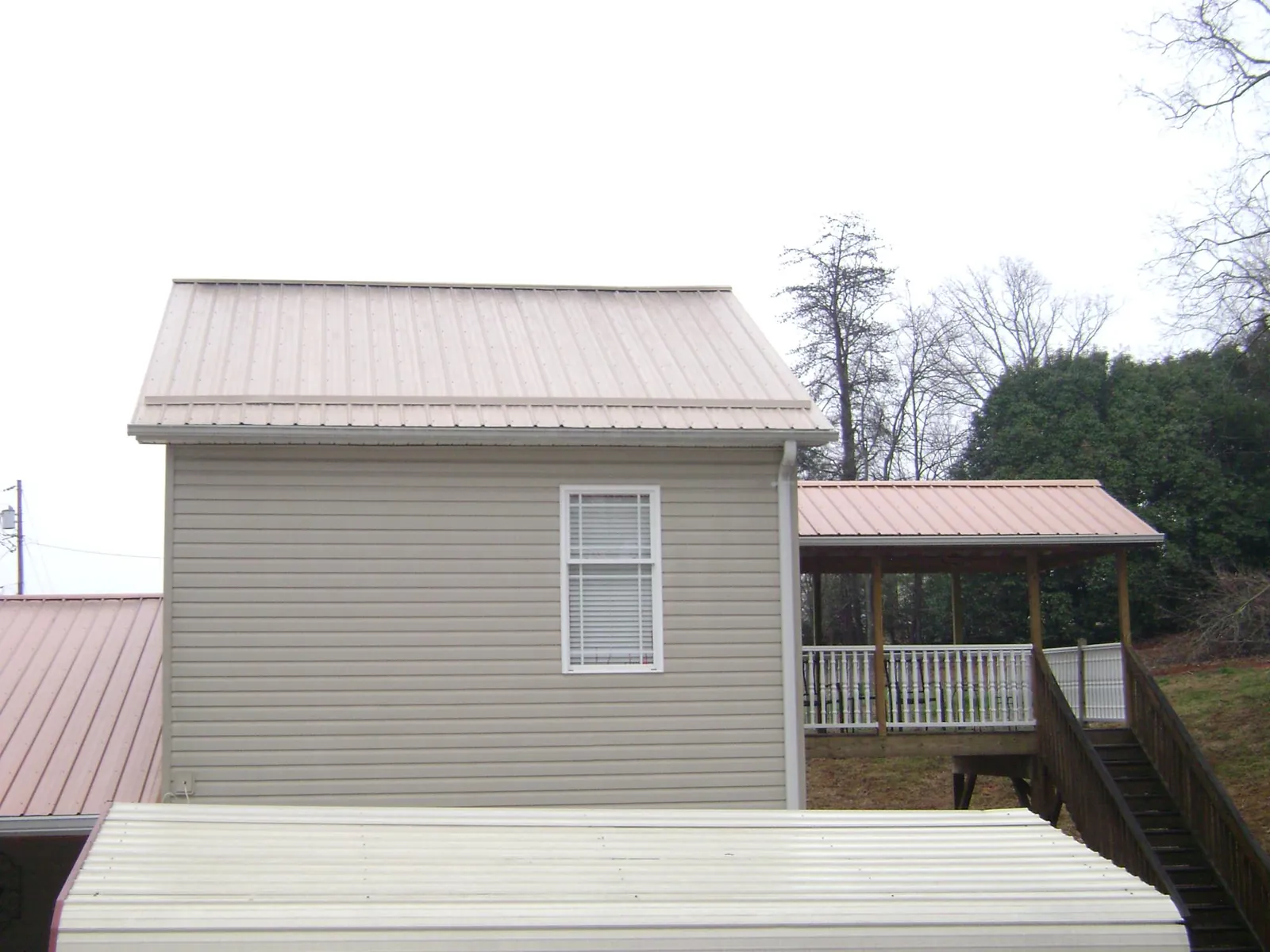 Tan metal roofs on a two story addition and attached porch, from a Roof Replacement job in Sanbornton
