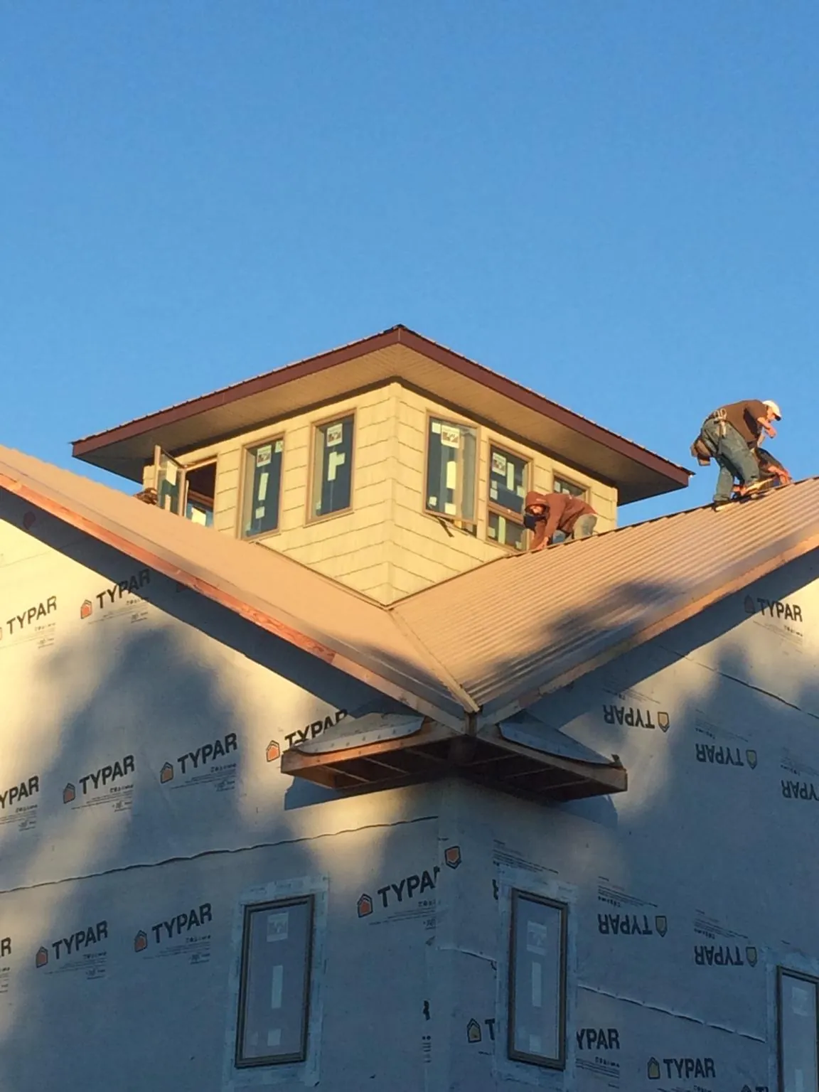 Roofers working around a rooftop cupola on a new metal roof at sunset — Roof Waterproofing in Sanbornton by Roofing Brothers